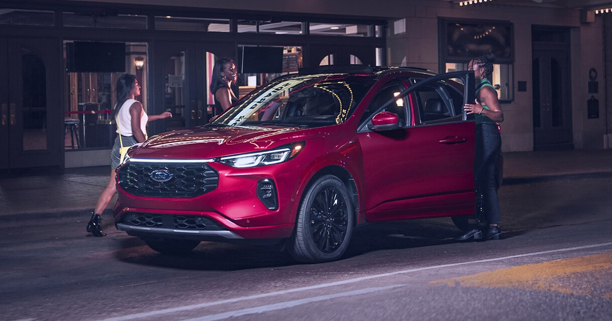 Three friends getting into their Ford Escape parked on the street at night.